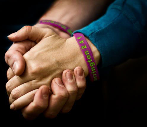 Two clasped hands wearing purple Harrington 241 awareness wristbands